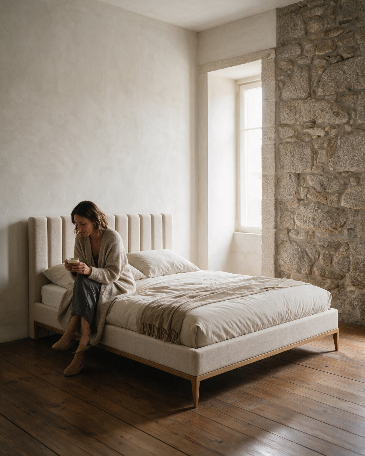 ECHO, cama estofada, num quarto de casa de pedra com uma mulher sentada com uma chávena de café