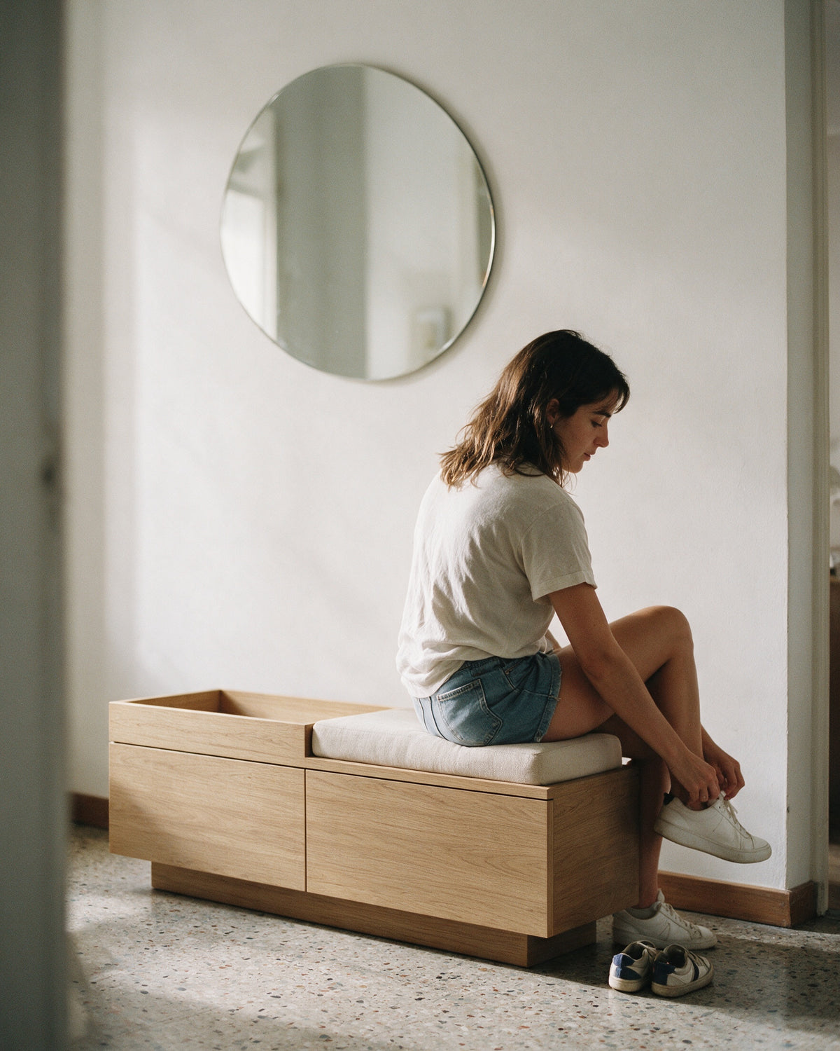 STRATA, banco em madeira de carvalho, num hall de apartamento dos anos 60 com uma pessoa sentada
