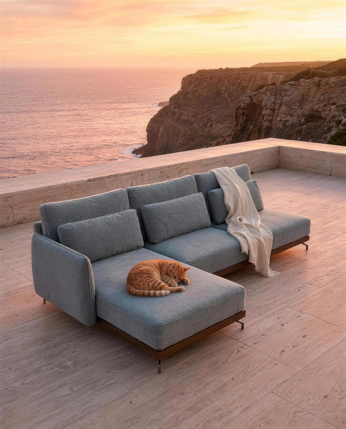 Sofá SLIM com chaise num terraço sobre a praia ao pôr do sol, com um gato a dormir na chaise